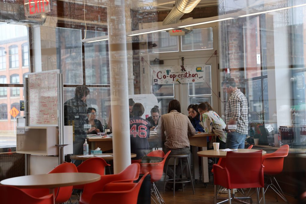 Worker Owners are gathered around a table for a project under a banner that reads Co-op-erathon.